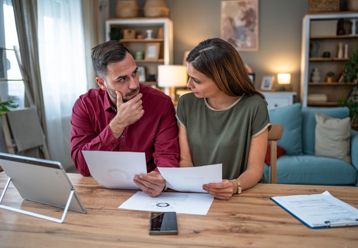 A couple sit at a table in their home looking at papers. 