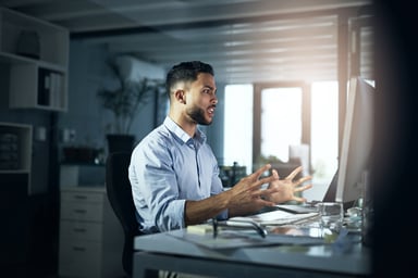 An angry person with hands outstretched looking at a computer monitor