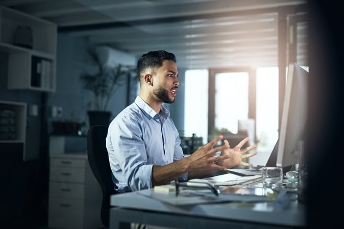 Angry man with arms outstretched while looking at computer monitor.