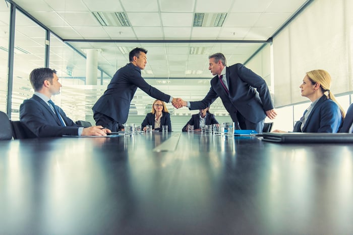 Two business people are shaking hands inside a boardroom. 