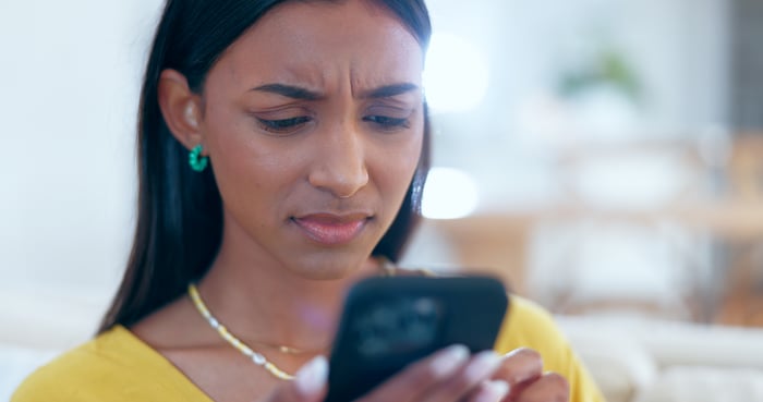 A person looking at a phone with a confused look.