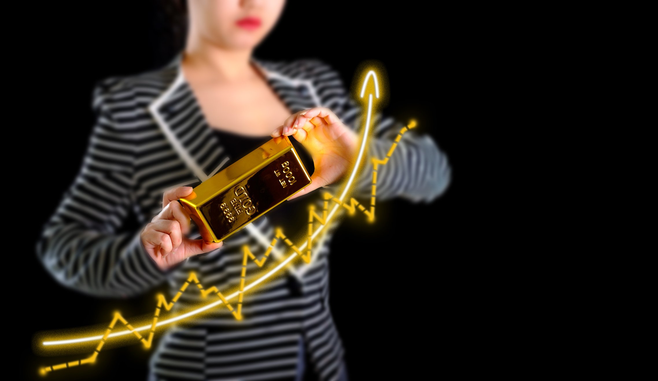 A person holding a gold bar next to a chart with an arrow pointed up.