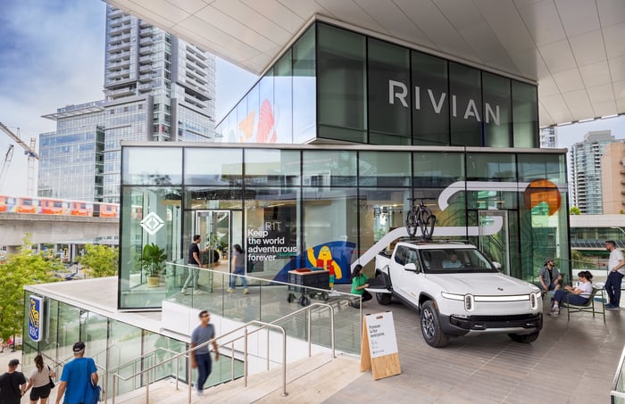A white truck at a Rivian building with people around it.