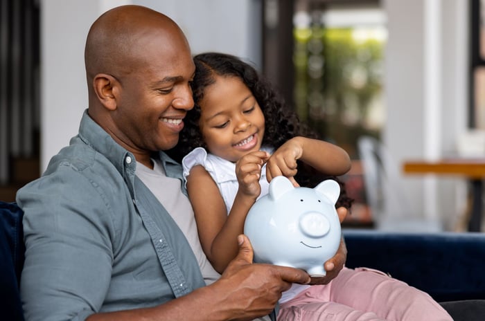 An adult and child putting money into a piggy bank.