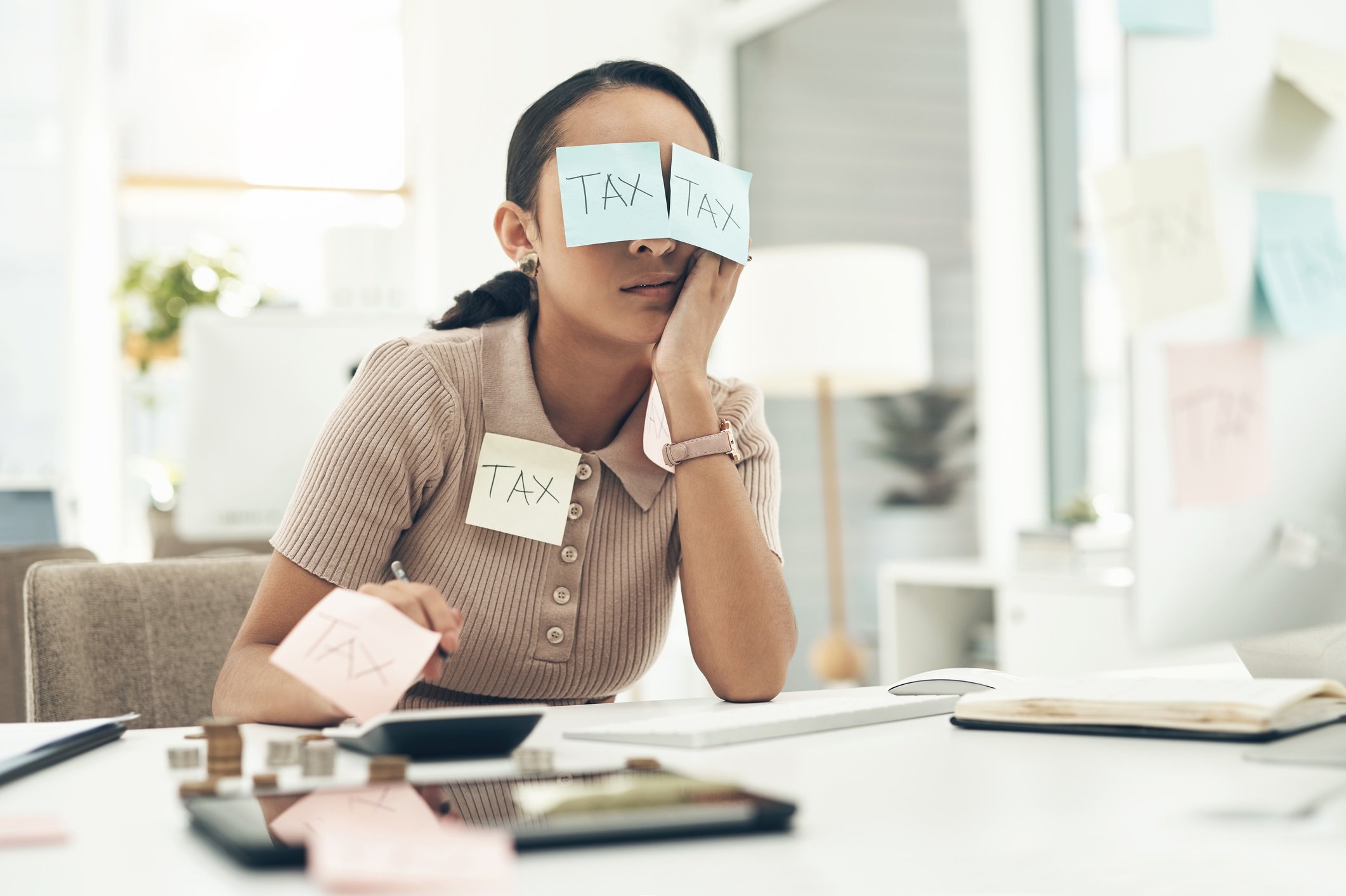 businesswoman covered in sticky notes while working on her taxes in an office
