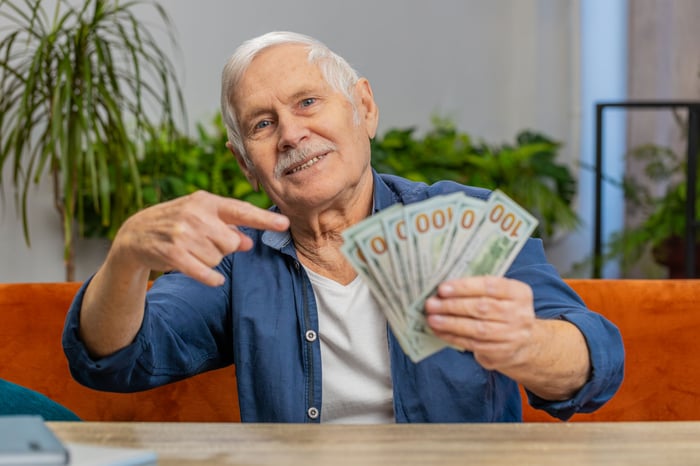 Older investor showing several hundred dollar bills in hand.