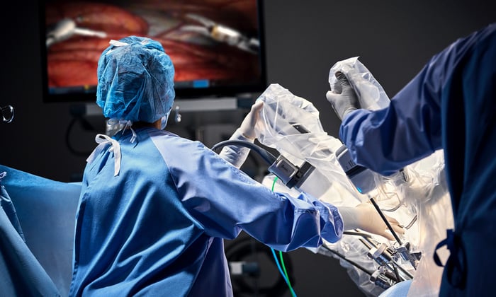 A healthcare professional helps during a surgical procedure, with surgical drapes covering the equipment in the background.