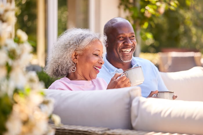 Smiling couple holding coffee mugs sitting on patio.