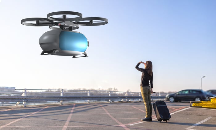 Person with suitcase looks up at a hovering air taxi.