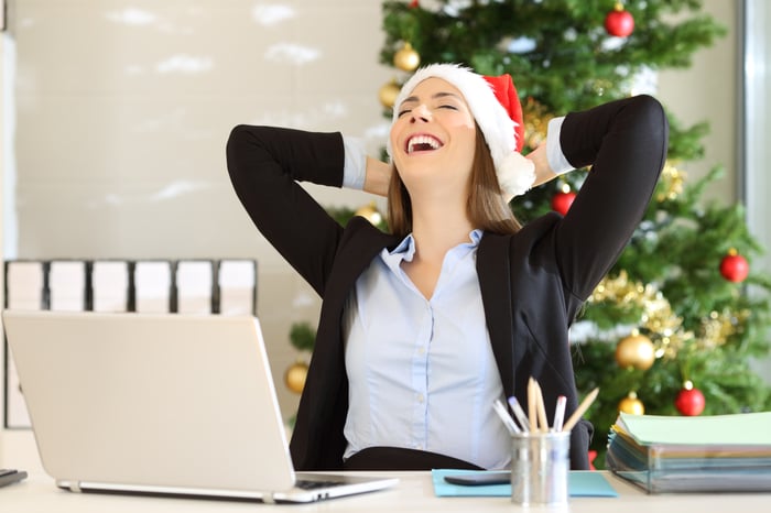 A happy person wearing a Santa hat and sitting at their computer in front of a Christmas tree.