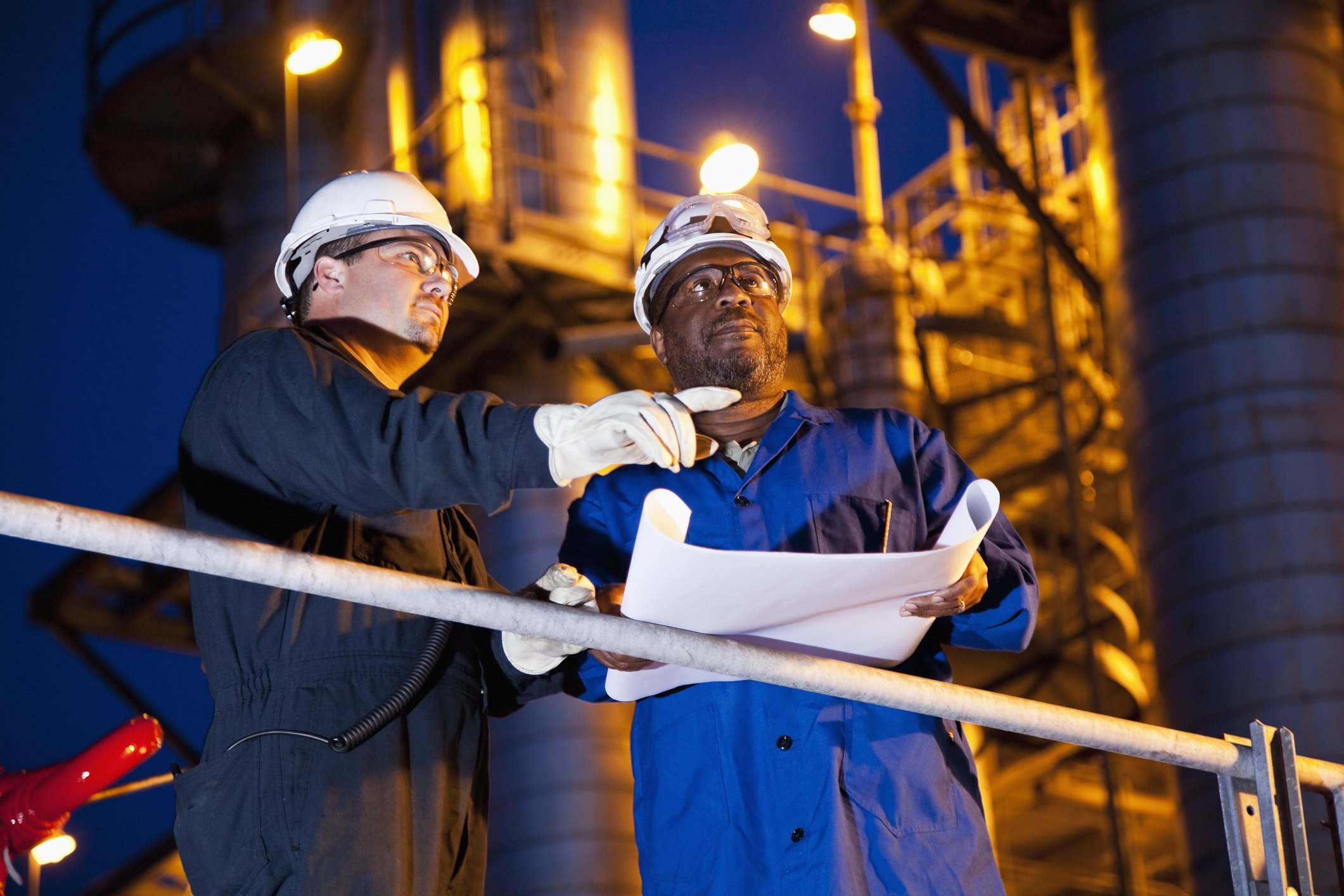 Two people look at plans at a refinery at night.