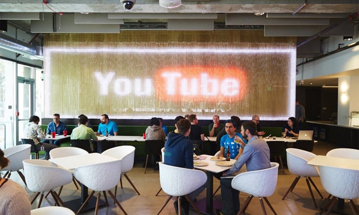 A YouTube office space with people sitting and a large YouTube logo in the background.