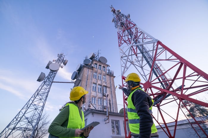 Two workers looking up at cellular towers.