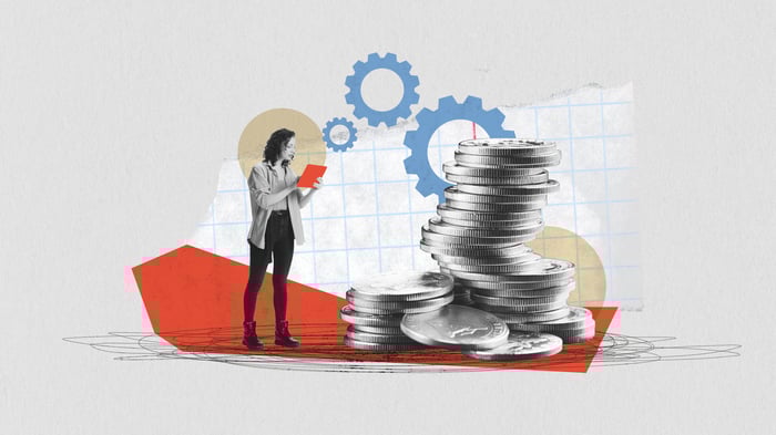 A person holding a tablet stands a short distance away from a tall pile of coins.