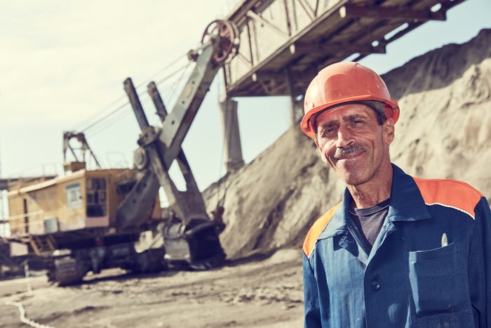 Smiling mine worker in front of a heavy excavator at a mining operation.