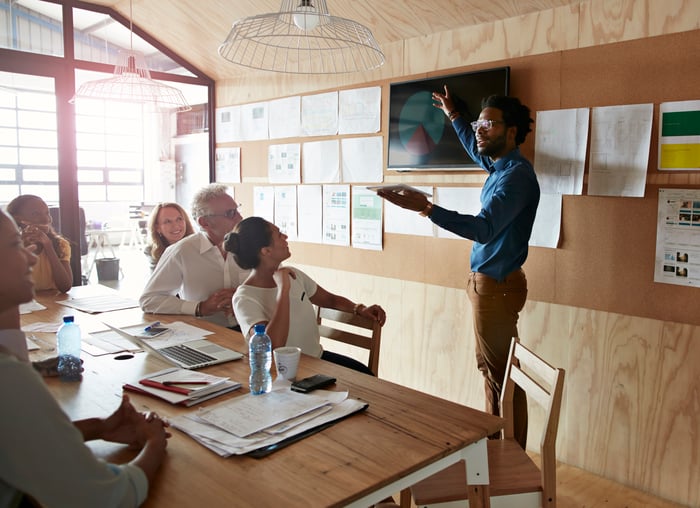 A group of people sitting at a table going over an advertisement on a wall panel.
