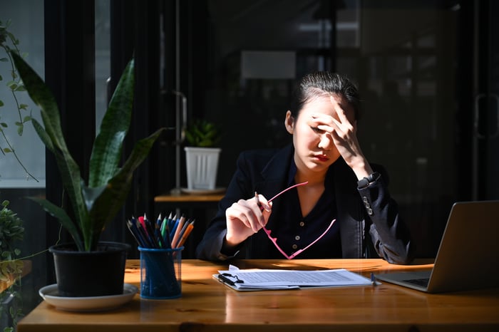 Person at desk rubs forehead while looking at a computer.
