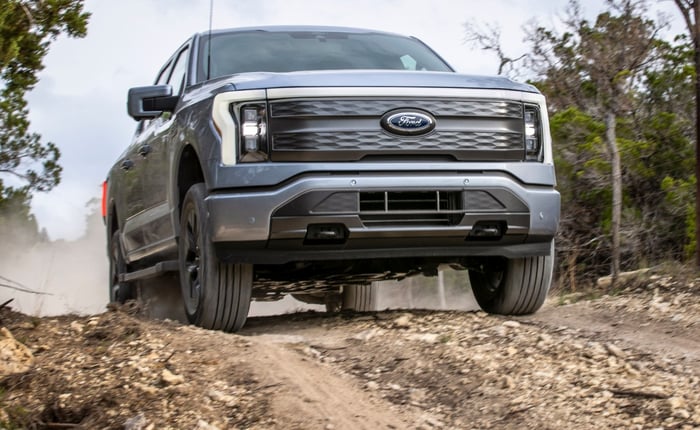 A Ford F-150 Lightning driving on a dirt road.
