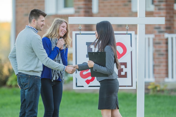 New homeowners are smiling as they shake hands with their real estate agent. 