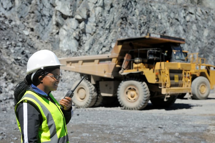 A person in protective gear standing by a giant truck in a mine site.