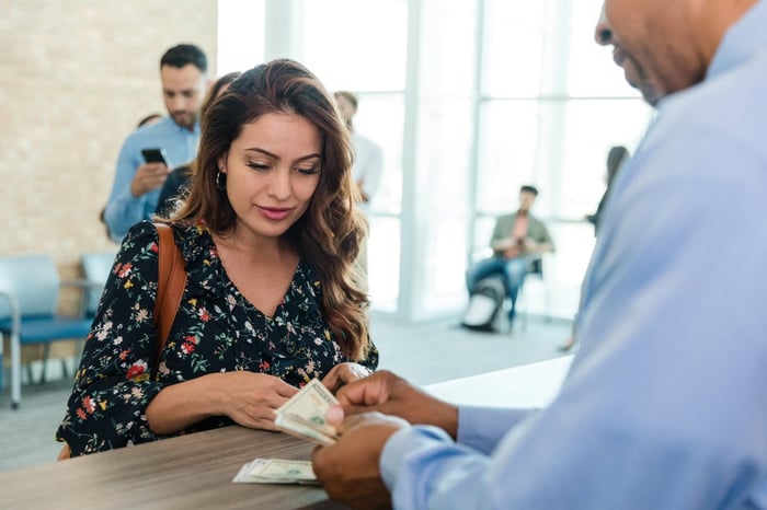 Young woman watching as a teller counts out cash. 