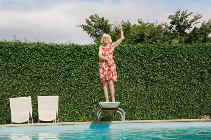 Older woman holding a dance pose, standing on a diving board. 