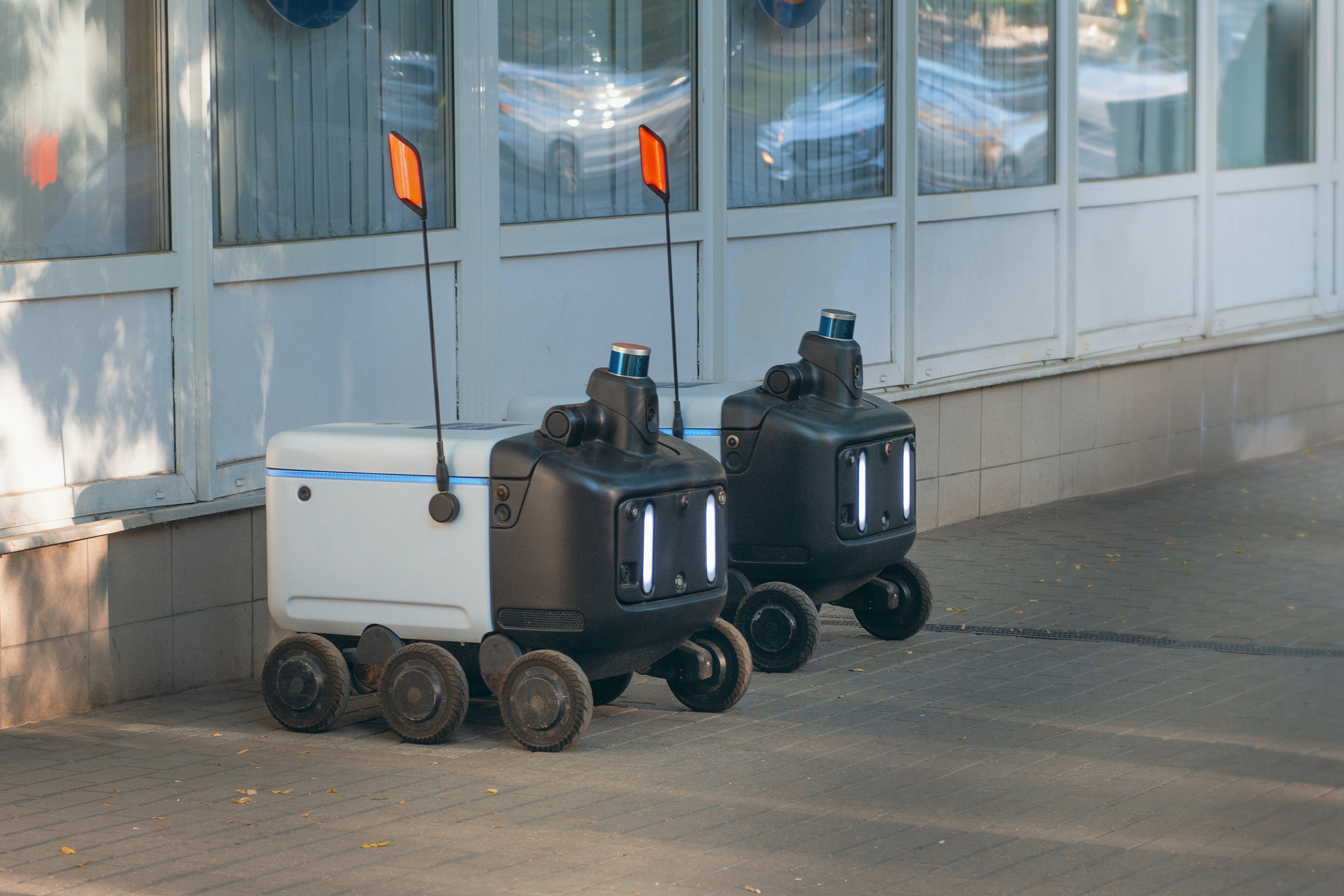 A pair of autonomous food delivery robots waiting on the sidewalk