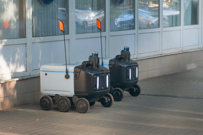 A pair of autonomous food delivery robots waiting on the sidewalk.