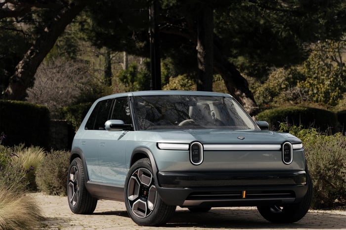 Rivian R2 in light blue sits in landscaped driveway.