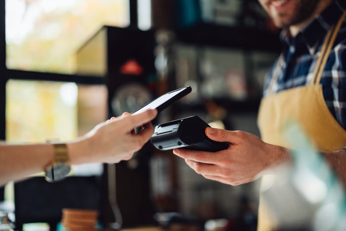 A person makes a digital payment with their phone in a coffee shop.