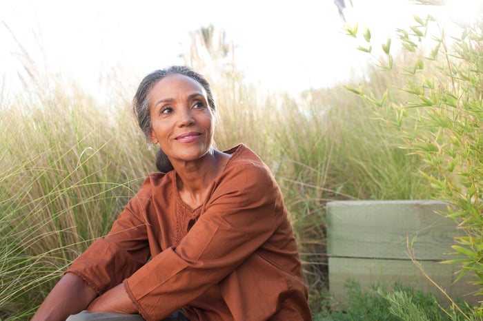 Someone is sitting outdoors in a brown top, smiling.