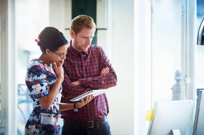 Two investors stand while looking down at a computer screen in an office.