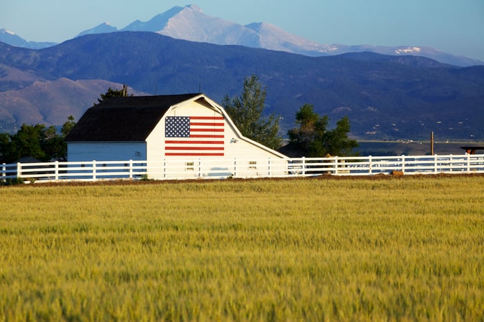 Looking across a field at a white barn featuring a large American flag.