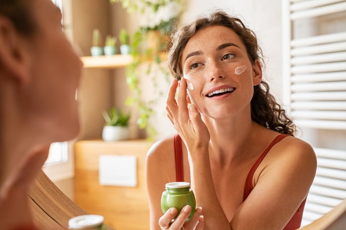 A person smiling while looking at themselves in the mirror and applying a skincare product.
