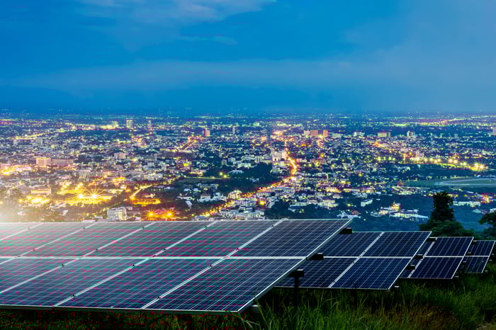 A city at dusk is powered by solar panels situated in the foreground.