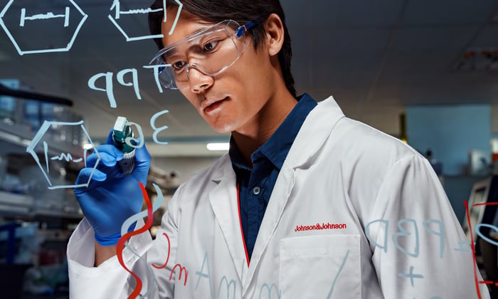 A person wearing a white coat with Johnson & Johnson above the pocket drawing on glass.