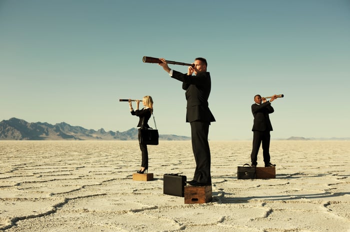Three business people with telescopes in desert.