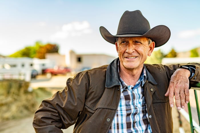 A farmer smiling while leaning on a fence at a farm.
