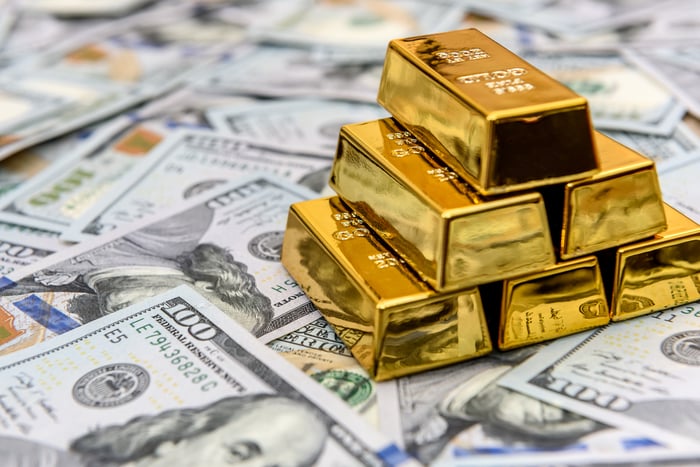 A stack of gold bars sitting on top of hundred-dollar bills.