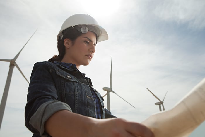 A person in work gear looking at blueprints with wind turbines in the background.