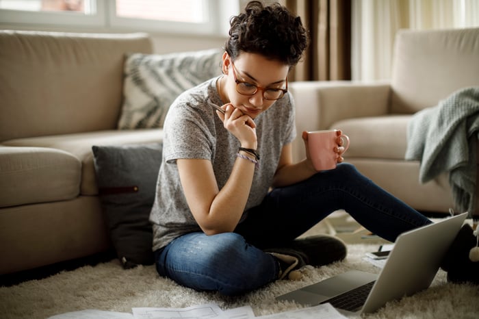 Person sitting on floor looking at documents and holding mug.