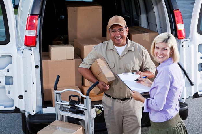 A delivery person handing a package from a delivery van to another person.