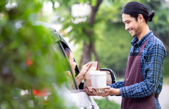 A smiling store worker delivers several drinks to a drive-thru customer.