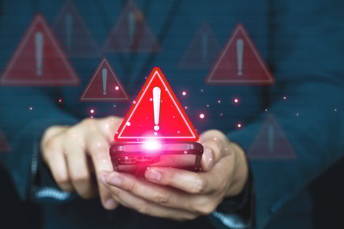 A person holding a phone with images of red triangular warning symbols in the foreground.