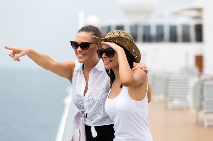 Two people stand on a cruise ship deck and look at something in the distance.