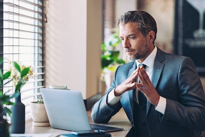A person in a suit wears a thoughtful expression while looking at a personal computer.