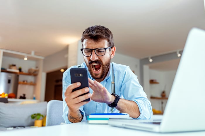 Investor wearing dress shirt and suspenders looking at smartphone in disbelief.
