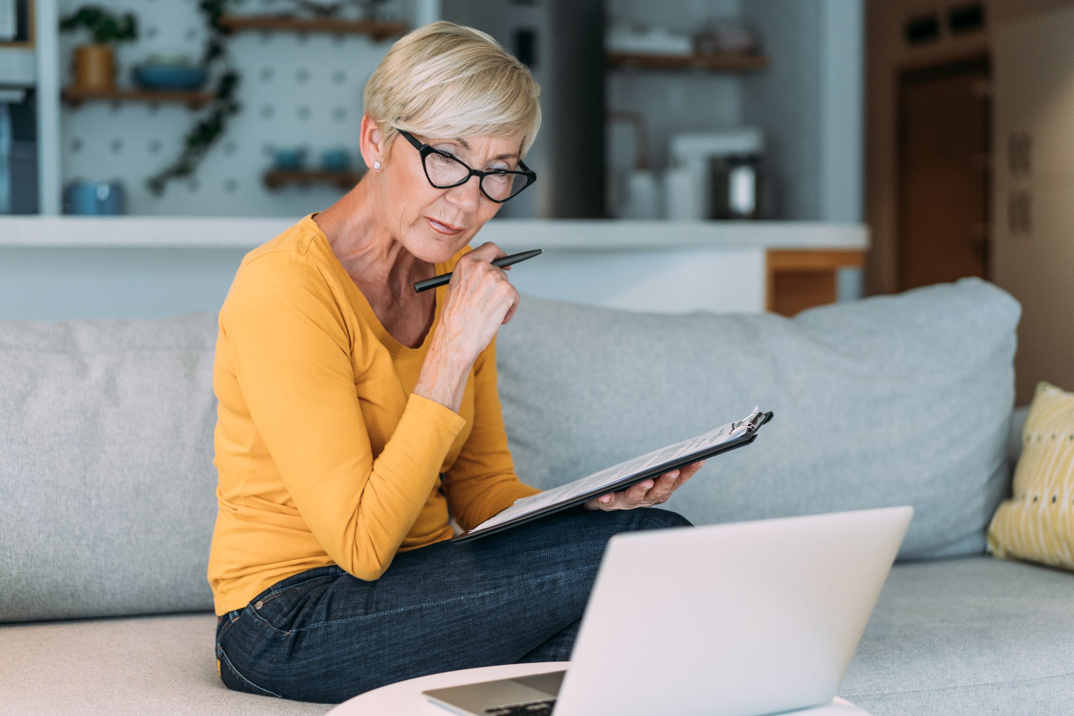 older woman at laptop holding clipboard GettyImages-1480979197