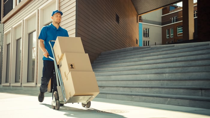 delivery driver wheeling packages on a dolly to a business. 