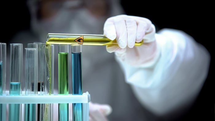 The hand of a researcher in full protective equipment pours colored liquids into test tubes.